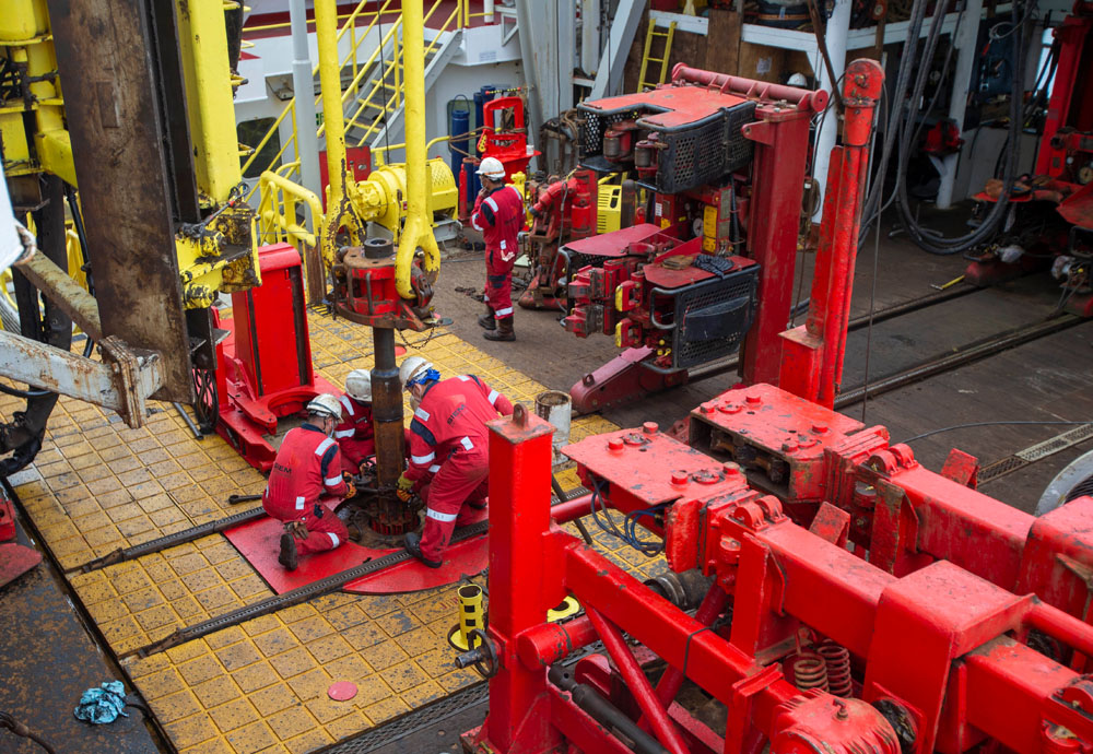 Red elevator around a tubular suspended from two yellow elevator links on the JOIDES Resolution drill floor.