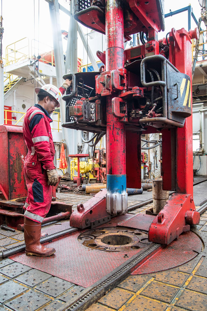Red iron roughneck positioned around a tubular on the JOIDES Resolution drill floor.