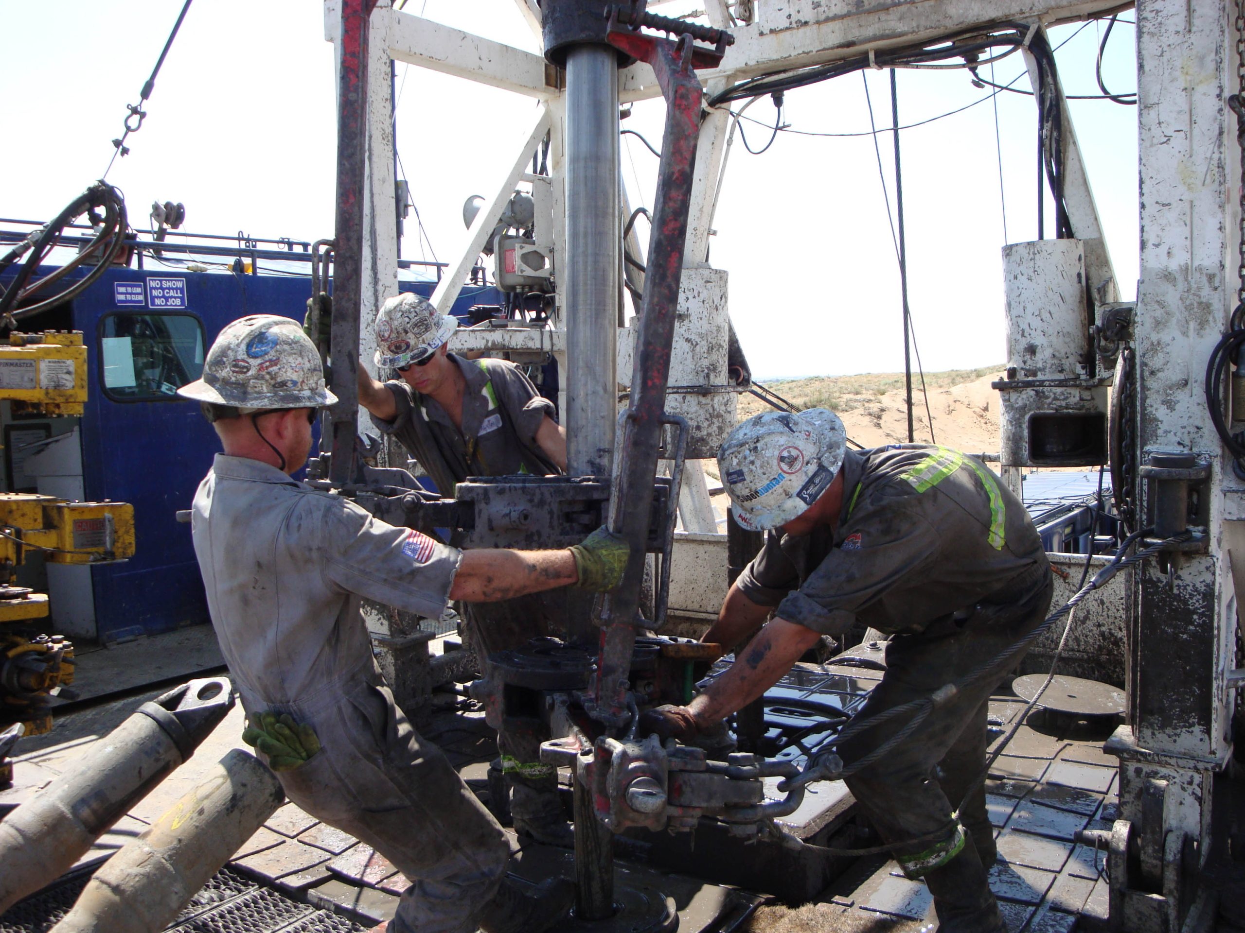 Drilling crew positioning manual tongs around a drill-pipe connection on a land rig.