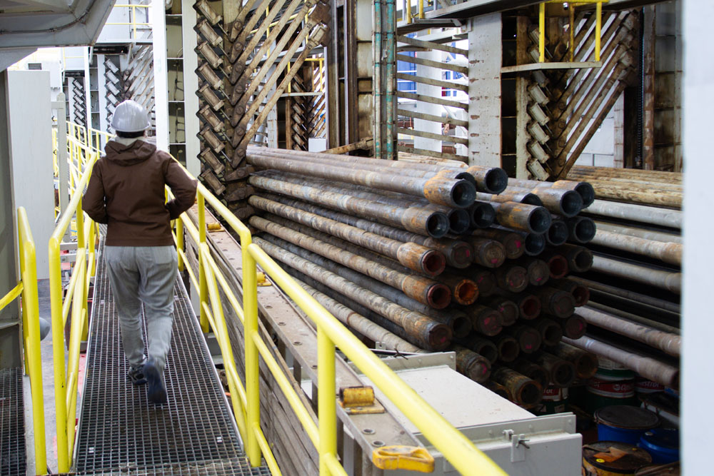 Horizontal tubulars stored in pipe racks beside a walkway on JOIDES Resolution.
