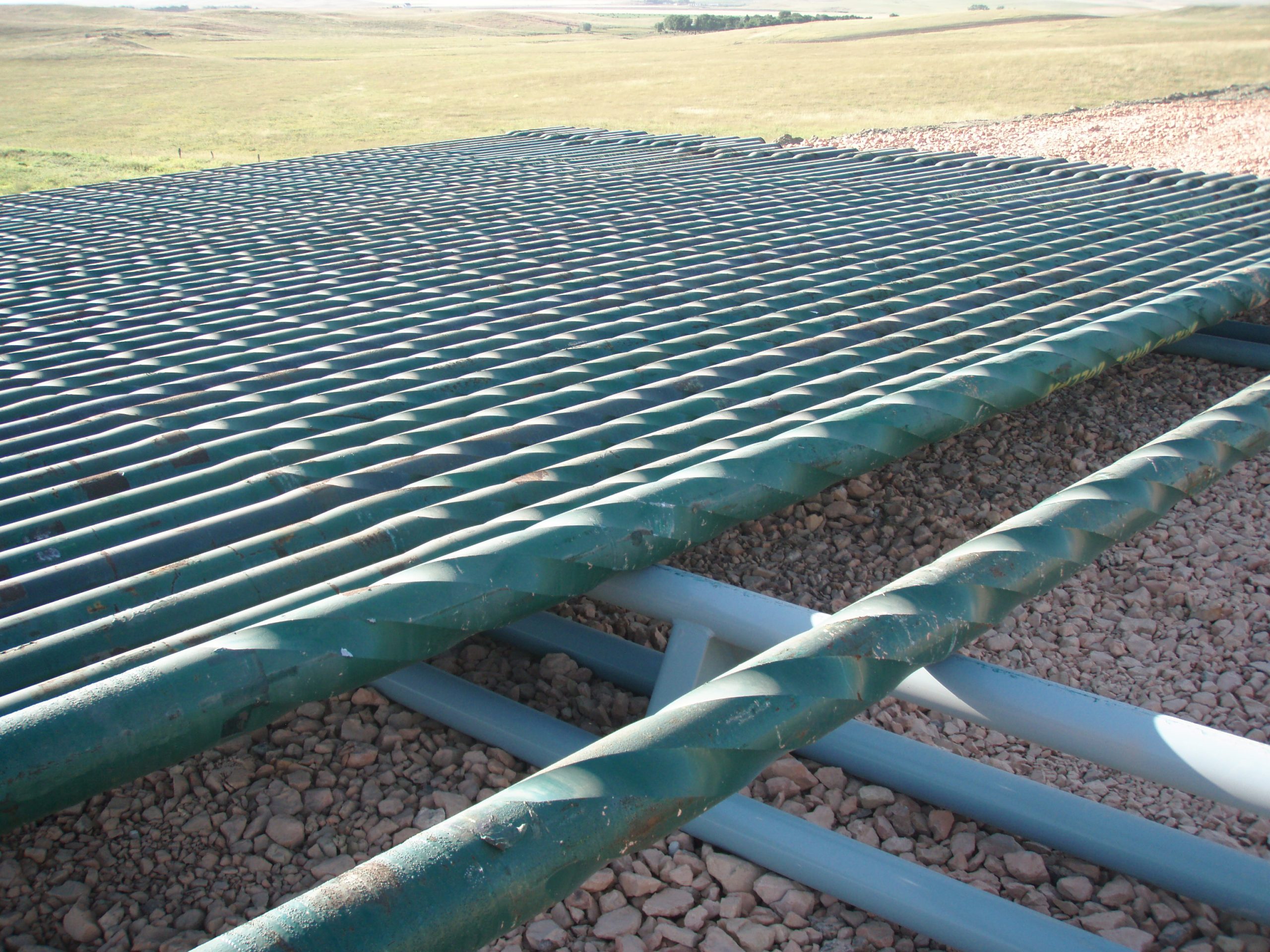 Green spiral drill collars arranged horizontally on a storage rack.